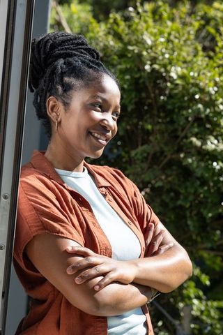 African woman leaning on doorframe smiling in garden sunlight casual lifestyle portrait