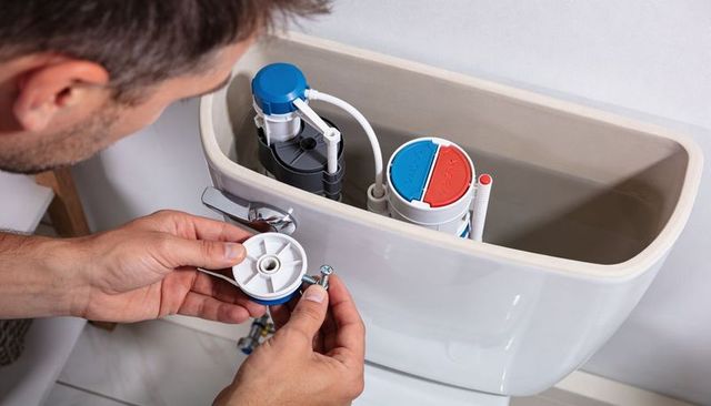 Man replacing toilet cistern flush valve and fitting replacement part with screw and wrench
