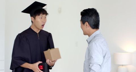 Surprised Graduate Holding Gift Indoors with Friend