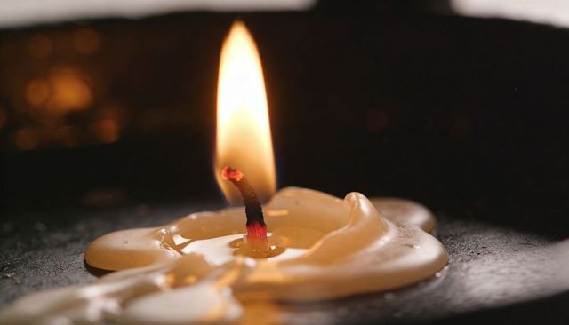 Melted wax pooling around glowing wick with warm amber flame closeup