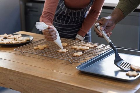 Couple decorating star cookies on cooling rack using piping bag and spatula