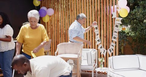 Multigenerational family hanging HAPPY BIRTHDAY banner on sunny backyard deck