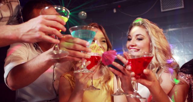 Group of friends enjoying a night out and celebrating with colorful cocktails in a lively nightclub. Ideal for promotions about nightlife, social events, party invitations, cocktail advertisements, and festive celebration themes.