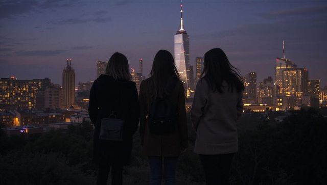 Three friends overlooking illuminated city skyline at twilight from urban hilltop lookout