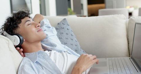 Young Man Relaxing with Laptop and Headphones on Comfortable Sofa
