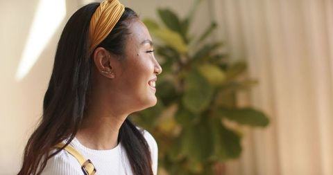Mid-adult asian woman smiling and looking to right wearing yellow headband and ribbed top
