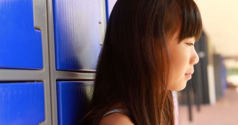 Contemplative Girl Standing by Blue Lockers in School Hallway