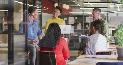 Woman leading data-driven meeting in modern open-plan office with glass charts