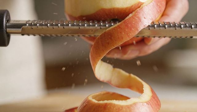 Hands peeling red apple with rotary peeler creating long spiral peel closeup food prep