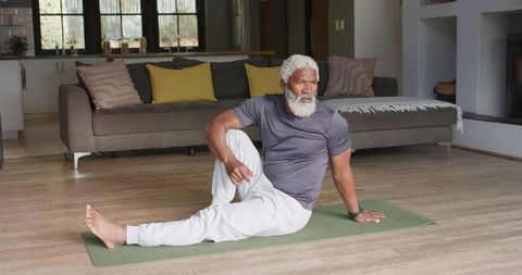 Mature man practicing yoga twist at home on green mat