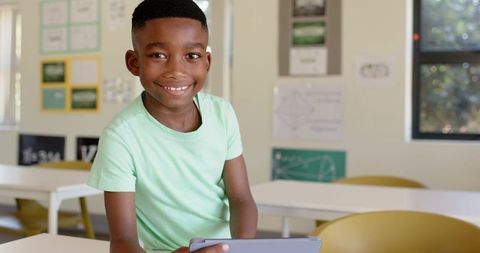 Smiling African American boy using tablet in bright classroom for digital learning