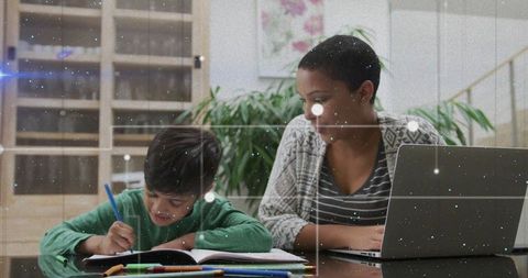Tutor guiding child doing homework at home table with laptop, notebook and cozy interior