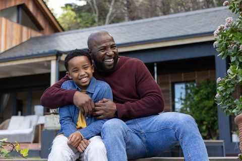 African american father embracing son on porch steps laughing together in sunlight