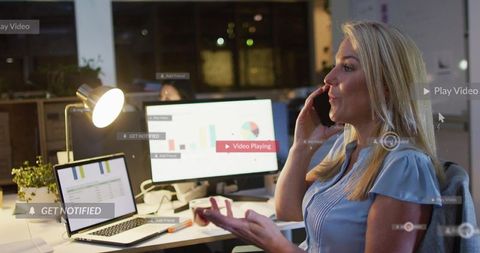 Businesswoman taking call while reviewing financial analytics on laptop at night