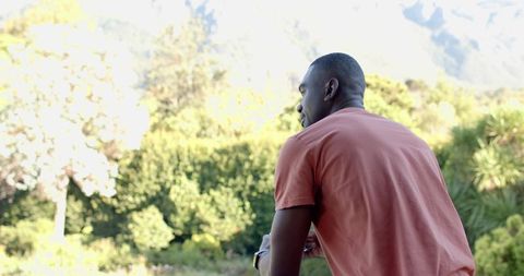 African american man leaning on railing, gazing at sunlit vista and mountains