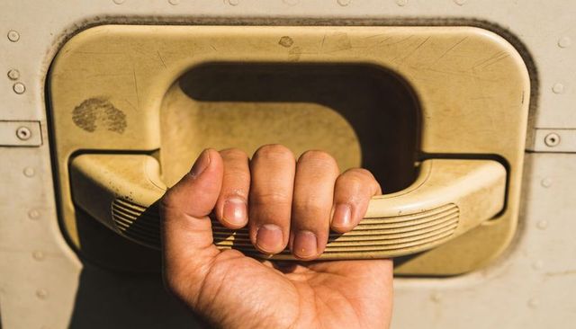 Gripping right hand pulling beige ribbed plastic handle on weathered painted metal panel