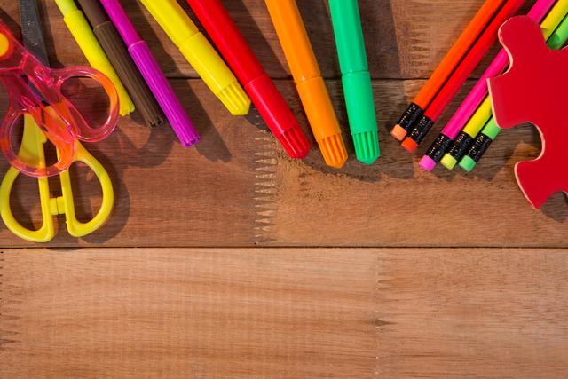 Close-up of bright stationery items like markers, pencils, and scissors spread on a wooden table. Ideal for use in educational materials, back-to-school promotions, organizational blogs, art and craft tutorials, and creative workspace design features.