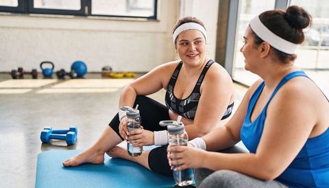 Women resting between sets on blue mat sharing water and smiling in modern gym