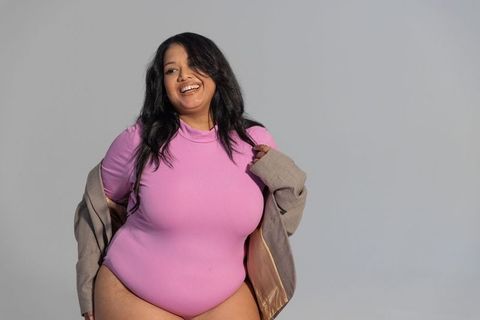 Smiling plus-size woman wearing pink high-neck bodysuit and draped beige jacket