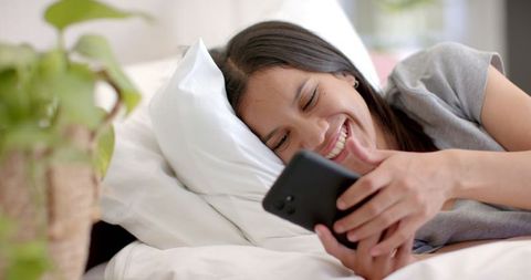 Teenage Girl Smiling While Using Smartphone in Bed