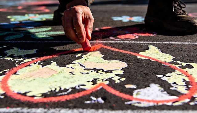 Artist outlining colorful chalk map heart on pavement with pink chalk