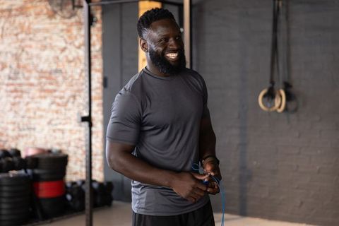 Smiling african american man holding blue jump rope in industrial gym