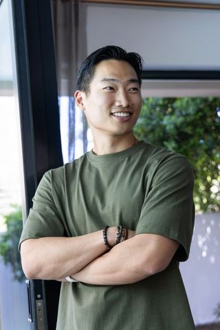 Asian man standing with arms crossed near sliding glass door smiling in casual home scene
