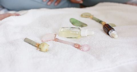 African american woman arranging facial rollers, gua sha stones and serums on white towel