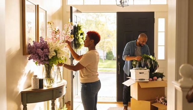 Couple decorating entryway with flowers and wreaths while unpacking boxes in bright foyer