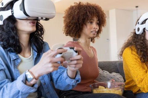 Young Women Playing VR Together on Couch Sharing Snacks and Reacting to Virtual Game