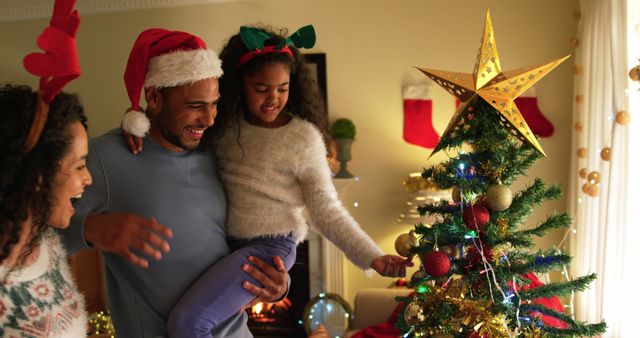 Biracial couple decorating a Christmas tree at home. They share a joyful moment with their biracial girl, embracing the festive spirit.