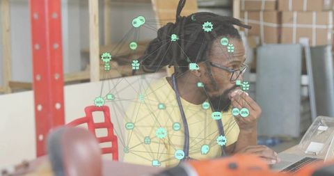 Focused craftsman with dreadlocks using laptop in workshop with healthtech network overlay