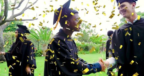 Graduates shaking hands amid gold confetti on campus lawn celebration