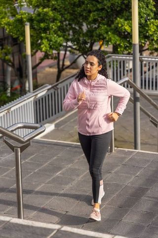Young woman climbing urban stairs during morning workout wearing pink jacket and smartwatch