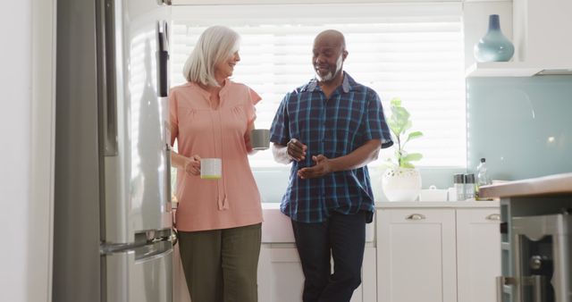 Senior couple joyfully conversing in a bright, modern kitchen. Highlights daily life interaction between older adults, perfect for promotions about retirement, healthy relationships, lifestyle, or home interiors.