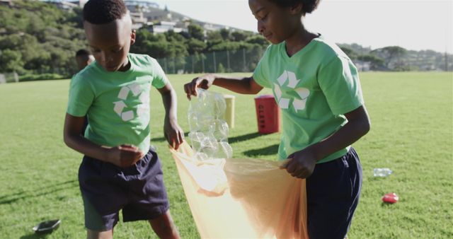 Children in green environment collecting plastic bottles into a large bag, promoting teamwork and eco-friendly practices. Useful for concepts related to sustainability, environmental education, community volunteering, and children's involvement in recycling efforts.