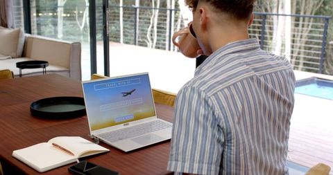Man drinking coffee while browsing travel page on laptop
