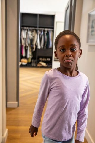 Pensive african american girl standing in hallway near open wardrobe wearing lavender top