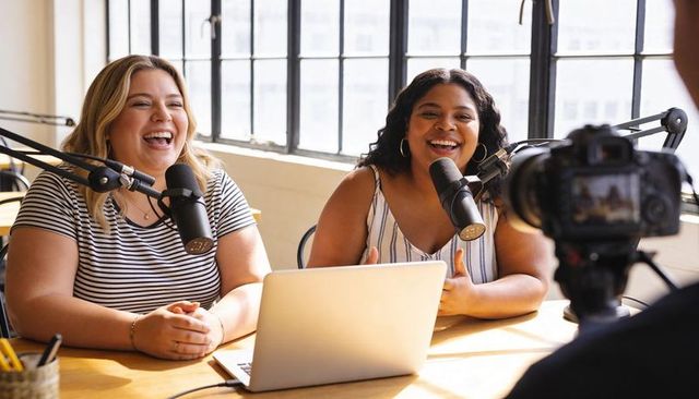 Laughing cohosts recording podcast in bright studio with laptop dslr and professional microphones