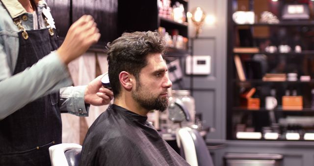 Man getting haircut in a modern barbershop, hairdresser using clipper on customer. Ideal for services showcasing grooming, haircut services, hairdressing techniques or barbershop promotions. Highlights personal care, grooming services, and hairstyling.