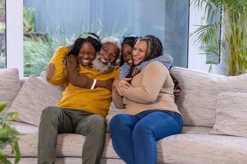 Multigenerational african american family hugging on couch smiling in cozy living room