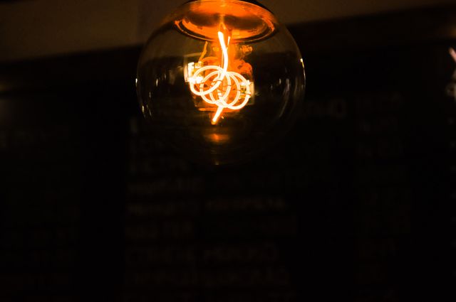 Close-up of a vintage Edison bulb showcasing its glowing filament in a dark room. Suitable for use in articles or blog posts about interior design, home decor, energy efficiency, and ideas for creating cozy atmospheres. Perfect for illustrating the concept of old-fashioned or retro lighting solutions.