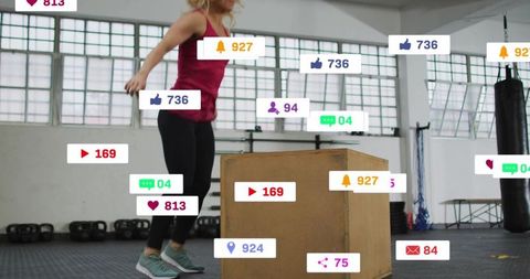 Female athlete jumping onto plyo box with social media notification overlays during gym workout