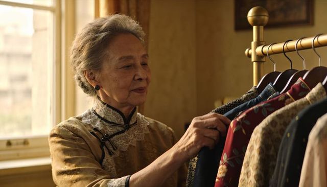 Elegant senior asian woman inspecting embroidered brocade jackets on brass clothing rack