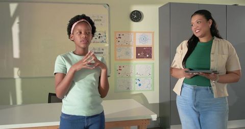 Youth student presenting while teacher holding tablet and smiling in classroom