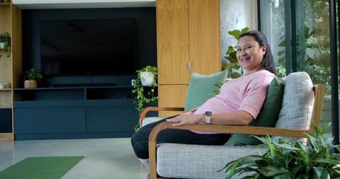 Mature african woman relaxing in modern living room wearing pink top and smartwatch