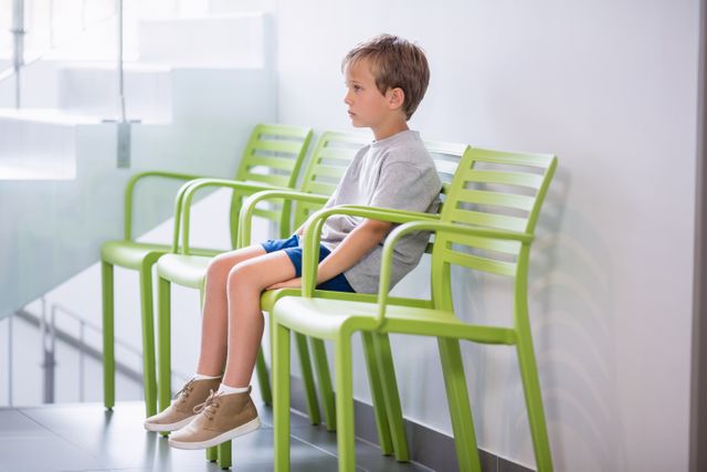Upset boy sitting on chair in corridor at hospital