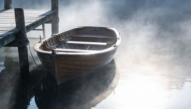 Floating wooden rowboat resting beside weathered dock in misty morning light