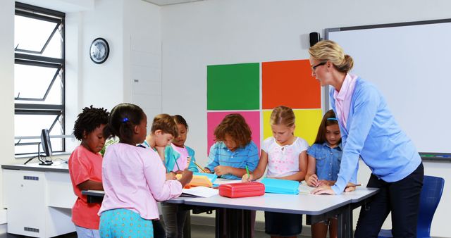 Teacher guiding group of diverse elementary school students during classroom activity, focusing on teamwork and interaction. Bright, colorful classroom with modern design elements. Ideal for educational content, school brochures, and materials promoting interactive learning and diversity.