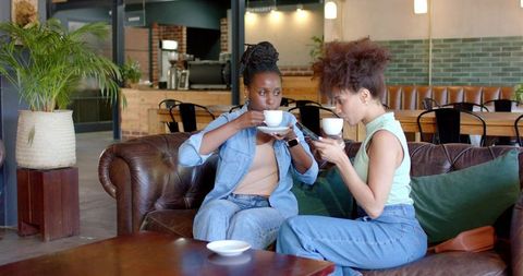 African American Women Enjoying Coffee and Chatting on Leather Couch in Urban Cafe Lounge